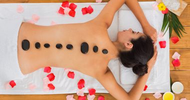 Black marble stone massage in spa. Top view of beautiful girl with stones on back and rose petals in wellness center. Pretty woman relaxation procedure, attractive young indian girl in beauty parlor.